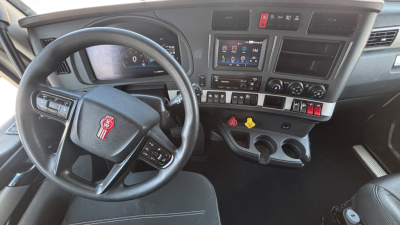 Truck interior dashboard of a Kenworth T680 showing steering wheel with logo, center console with touchscreen display, various gauges, climate controls, and gear shifter.