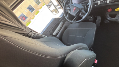 Kenworth T680 interior driver's seat and dashboard view from open door showing steering wheel and control panel.