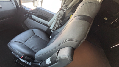 Kenworth T680 cab interior showing driver's seat and passenger seat with seat belts and dashboard.