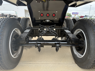 Trailer rear view showing dual rear axles with heavy-duty suspension and differential housing, black components, tires, and hydraulic lines.