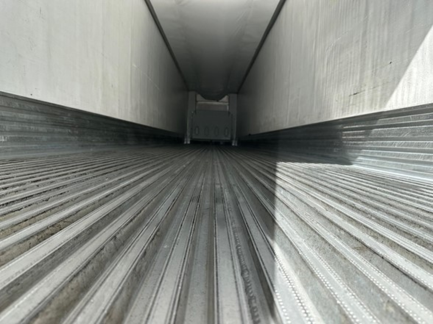 Trailer interior showing long metal floor with ribbed grooves and side walls, empty cargo area, perspective toward far end.