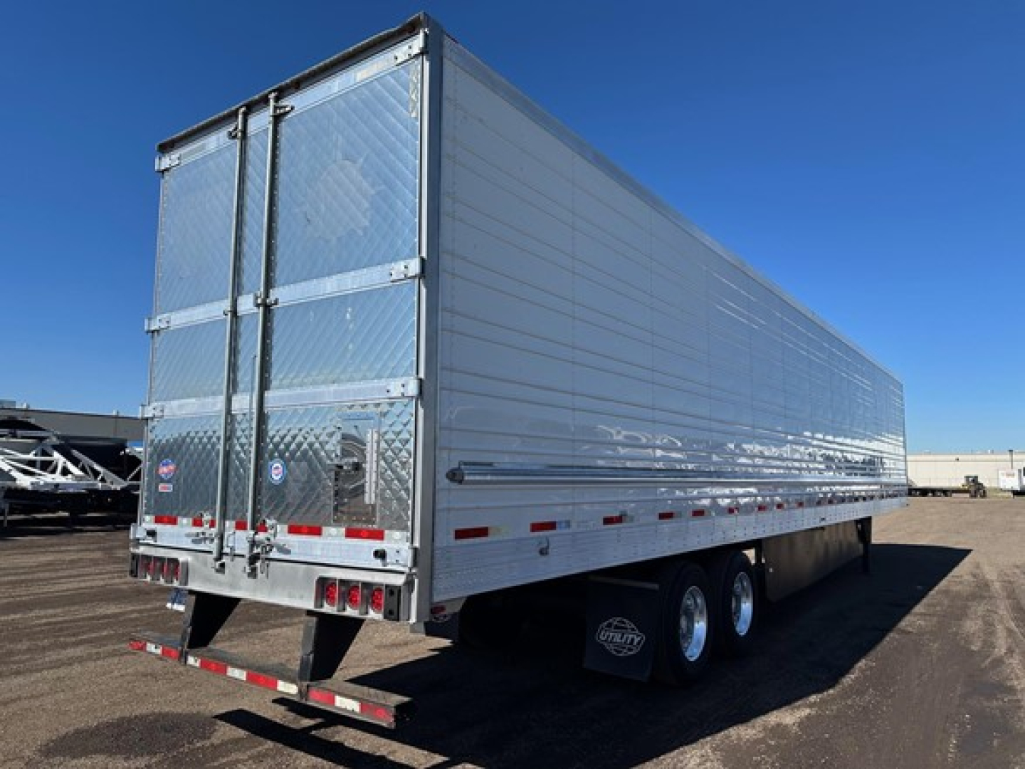 Trailer side and rear view showing a silver Utility S-700 refrigerated trailer with triple axles, rear doors, and reflective safety markings.