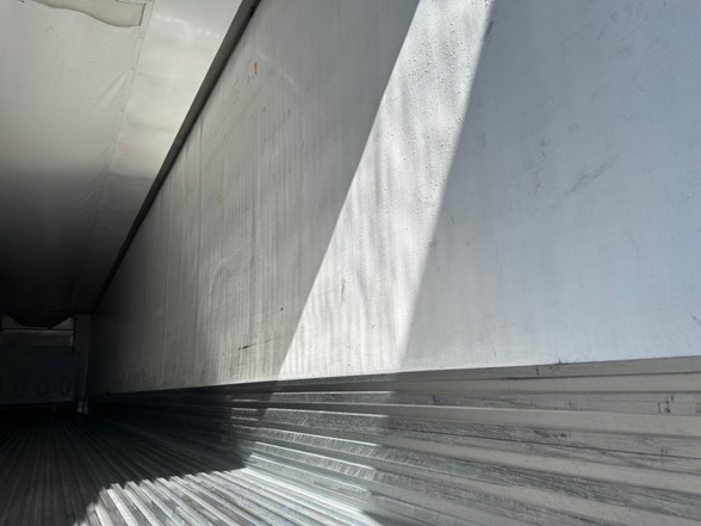 Trailer interior showing aluminum side walls and ribbed floor of a Utility S-700 reefer trailer, with light and shadows along the seam.
