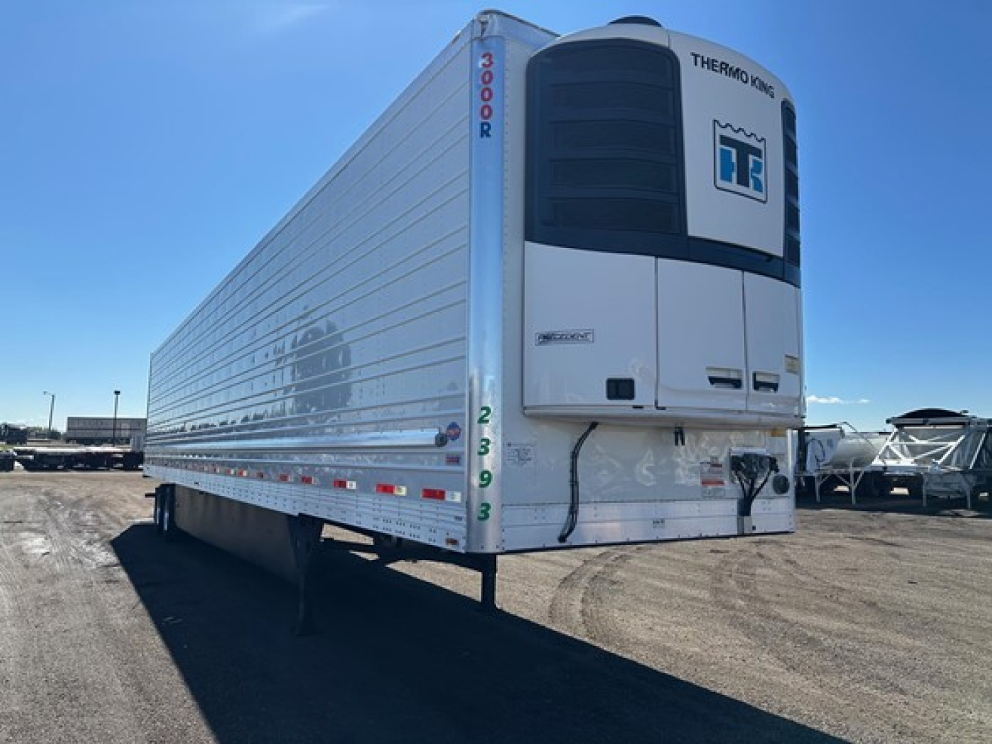 Trailer side and front of a 2023 Utility S-700 reefer trailer with Thermo King unit, silver ribbed aluminum walls, and vertical blue-yellow markings.