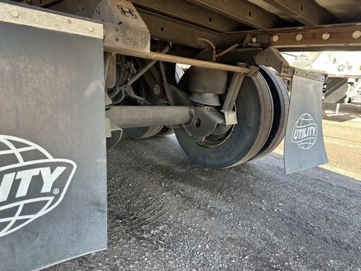 Reefer trailer undercarriage showing wheel hub, suspension, and Utility mud flaps with logo and spare components.