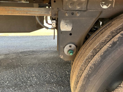 Trailer axle area of a 2023 Utility S-700 reefer trailer showing wheel, suspension arm, and green-botted component with dirt on tire surface.