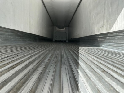 Trailer interior showing long metal floor with ribbed grooves and side walls, empty cargo area, perspective toward far end.