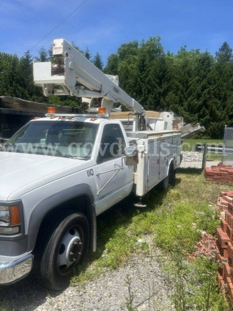 Truck with bucket lift utility body, white 2000 Chevrolet C/K 3500, side view showing hydraulic boom and utility compartments.