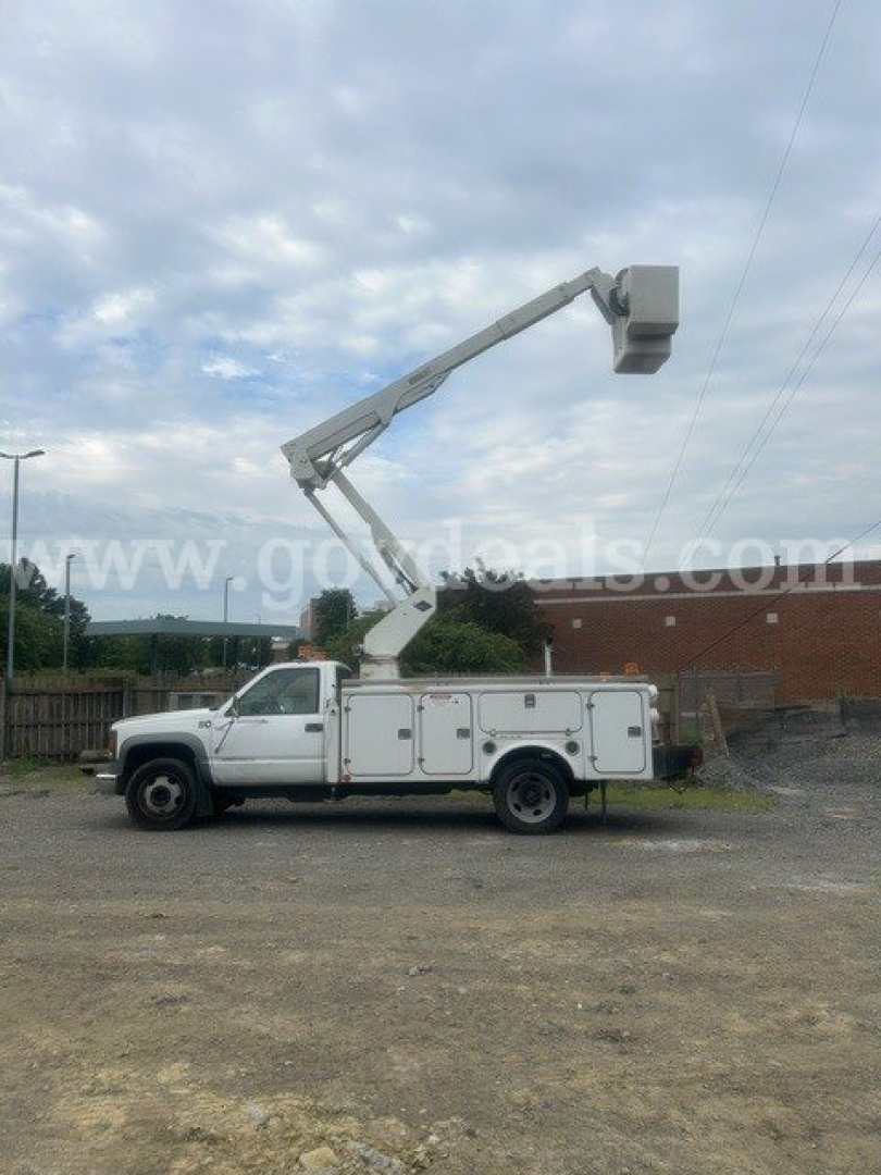 Utility bucket truck with insulated body and boom raised, white color, side cabinets visible.