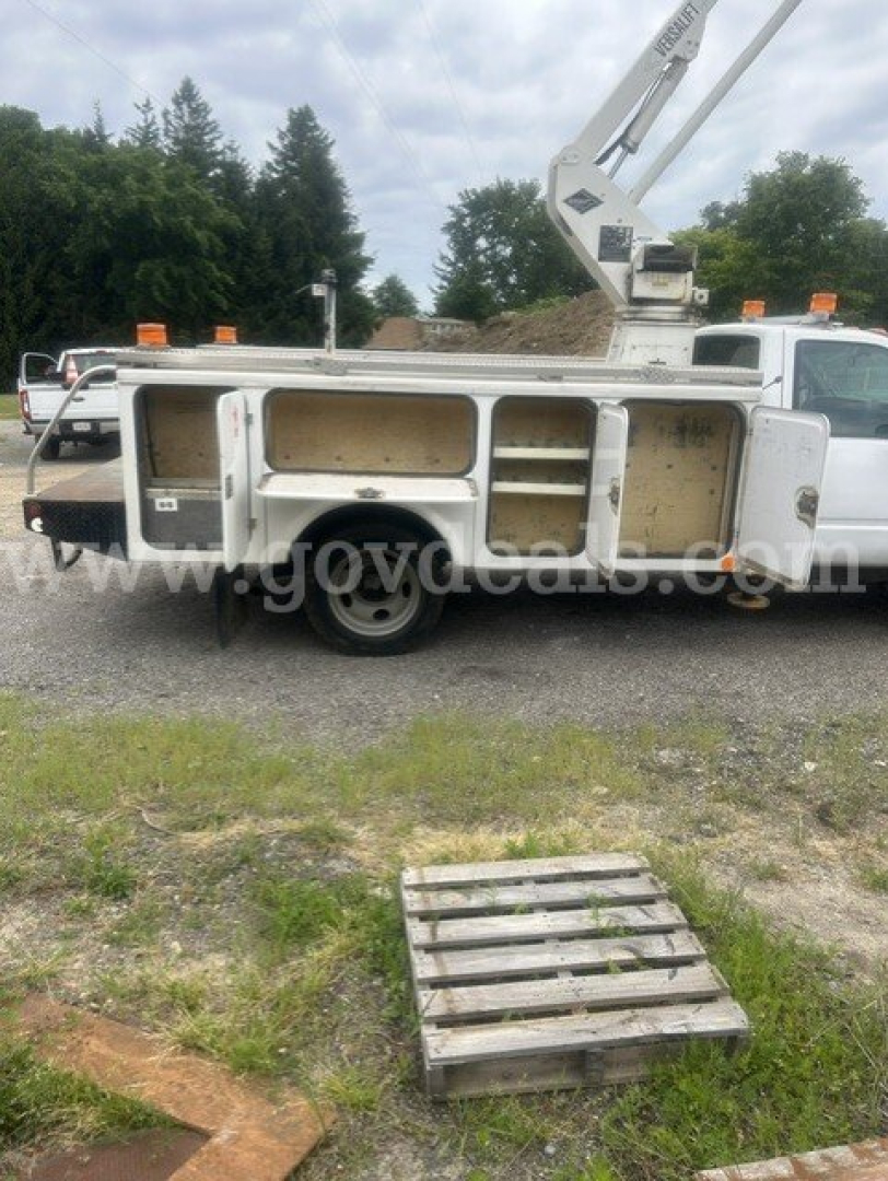Truck bed with multiple compartments and a crane on a utility truck. Visible labels include a white door label on the side near the wheel and an orange beacon.