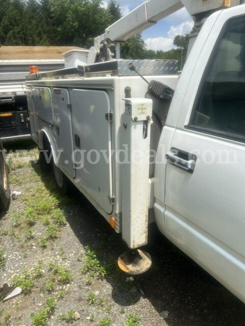 Truck utility body on a 2000 Chevrolet C/K 3500 with utility bed and bucket lift, side view showing compartments and controls.