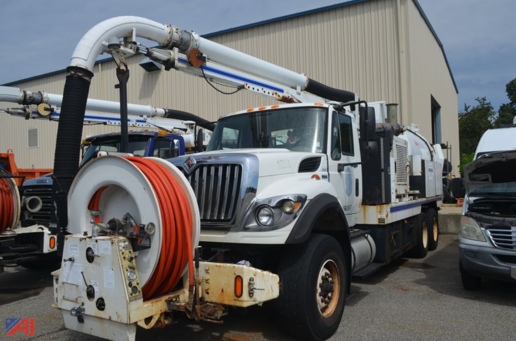 Vacuum truck with large reel and hose assembly mounted on a white International WorkStar 7400, front grille and cab visible, equipment yard background.