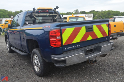 Rear view of a blue 2018 Chevrolet Silverado 2500HD pickup truck with reflective chevron tailgate pattern and utility equipment in a lot.