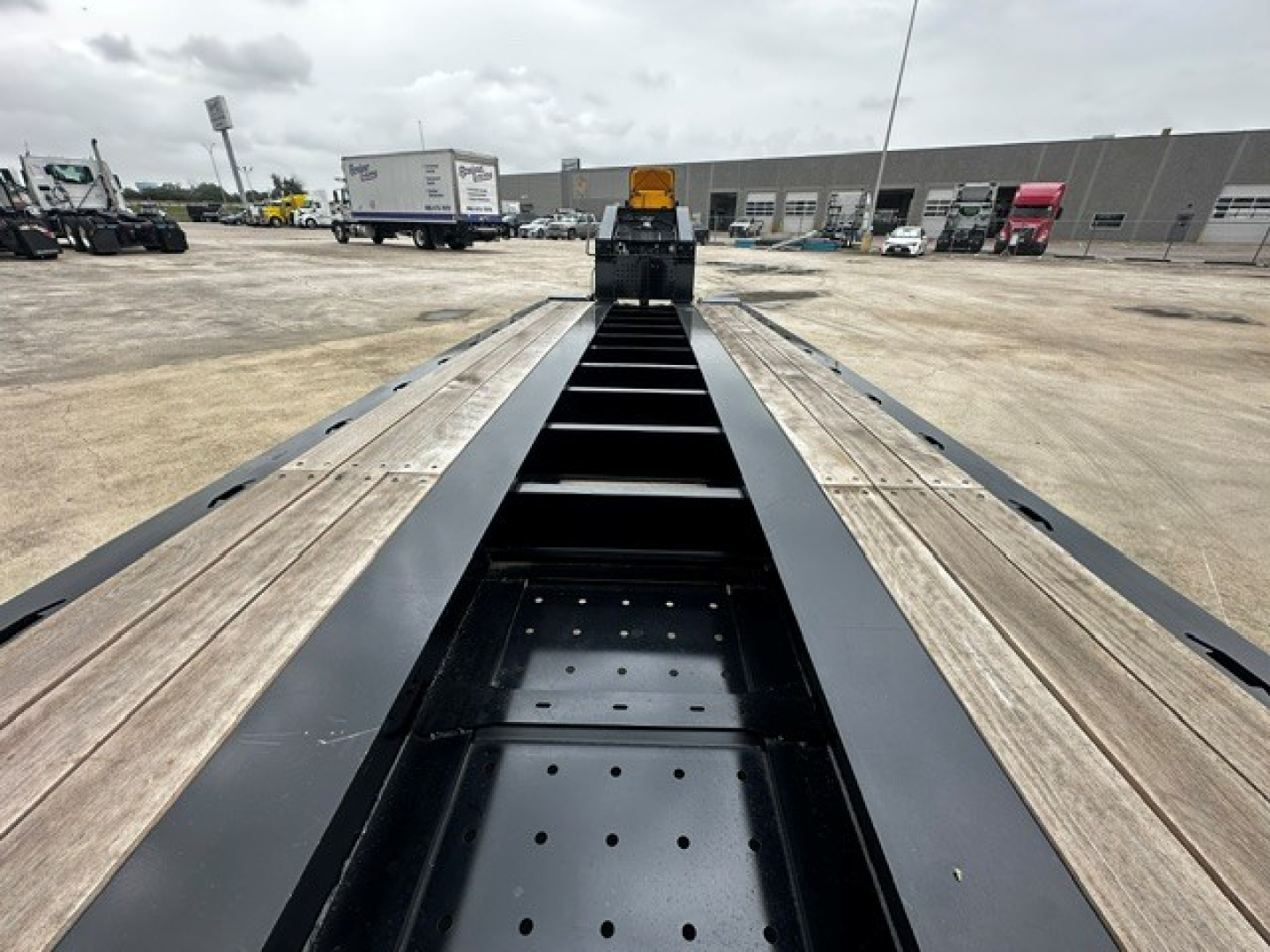 Trailer frame view showing central beam and leaf-spring style platform on Load King 604/5 SS SF lowboy trailer, with wooden deck planks and steel side rails.