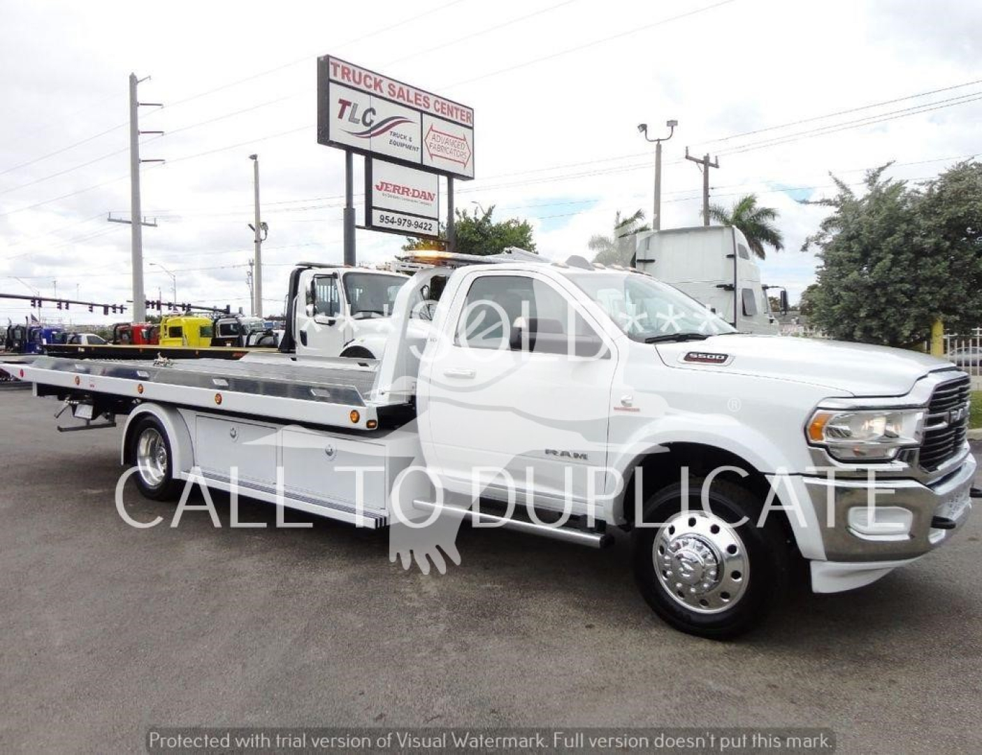 Ram 5500 rollback tow truck with flatbed and chrome wheels in a dealership lot.