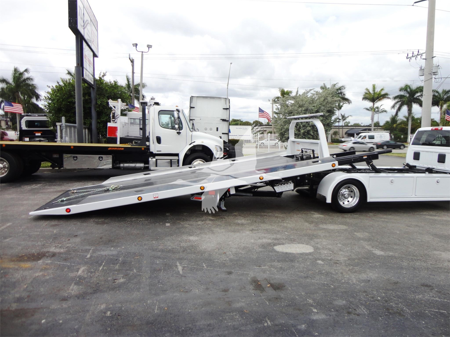 Ram 5500 HD SLT rollback truck with a lowered flatbed loading ramp and white cab, front view showing trailer bed and wheel position.