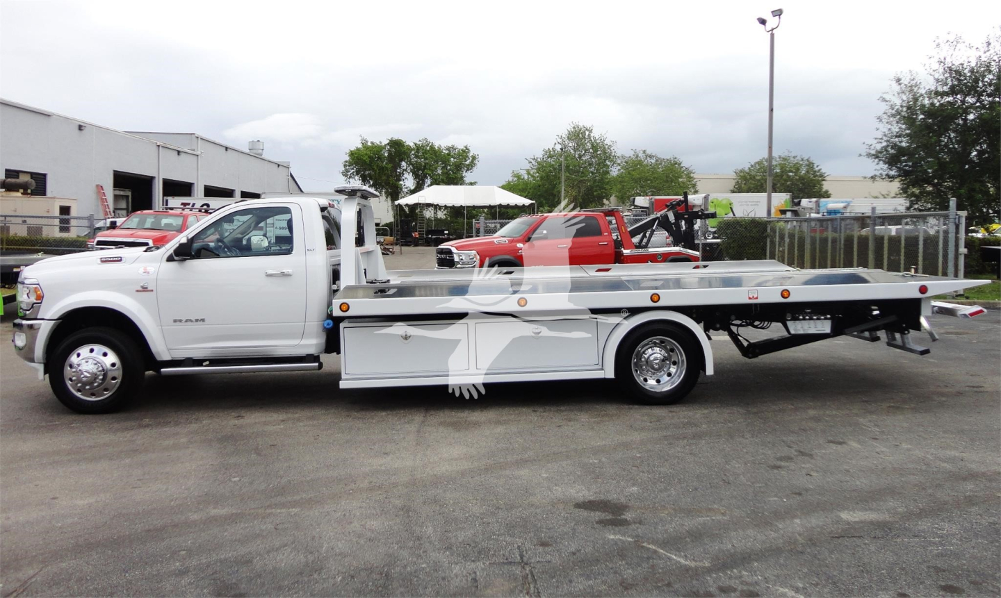 White 2023 Ram 5500 HD SLT rollback tow truck with flatbed, side view showing wheel and tow equipment.