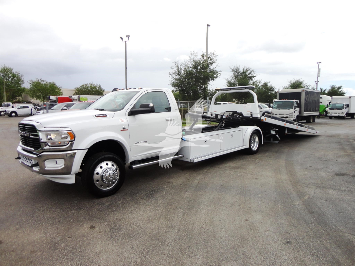 Ram 5500 HD SLT tow truck with rollback bed in a dealership lot, white cab, long wheelbase, image shows front-left side