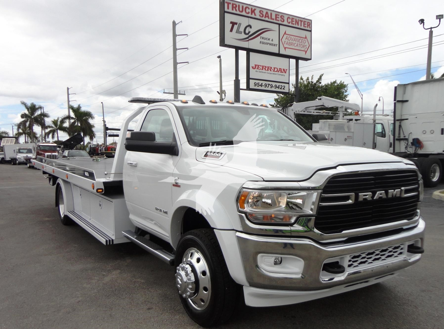 Ram 5500 heavy-duty rollback tow truck in white, front grille with RAM emblem, side view showing flatbed and dual rear wheel, dealership lot in background.