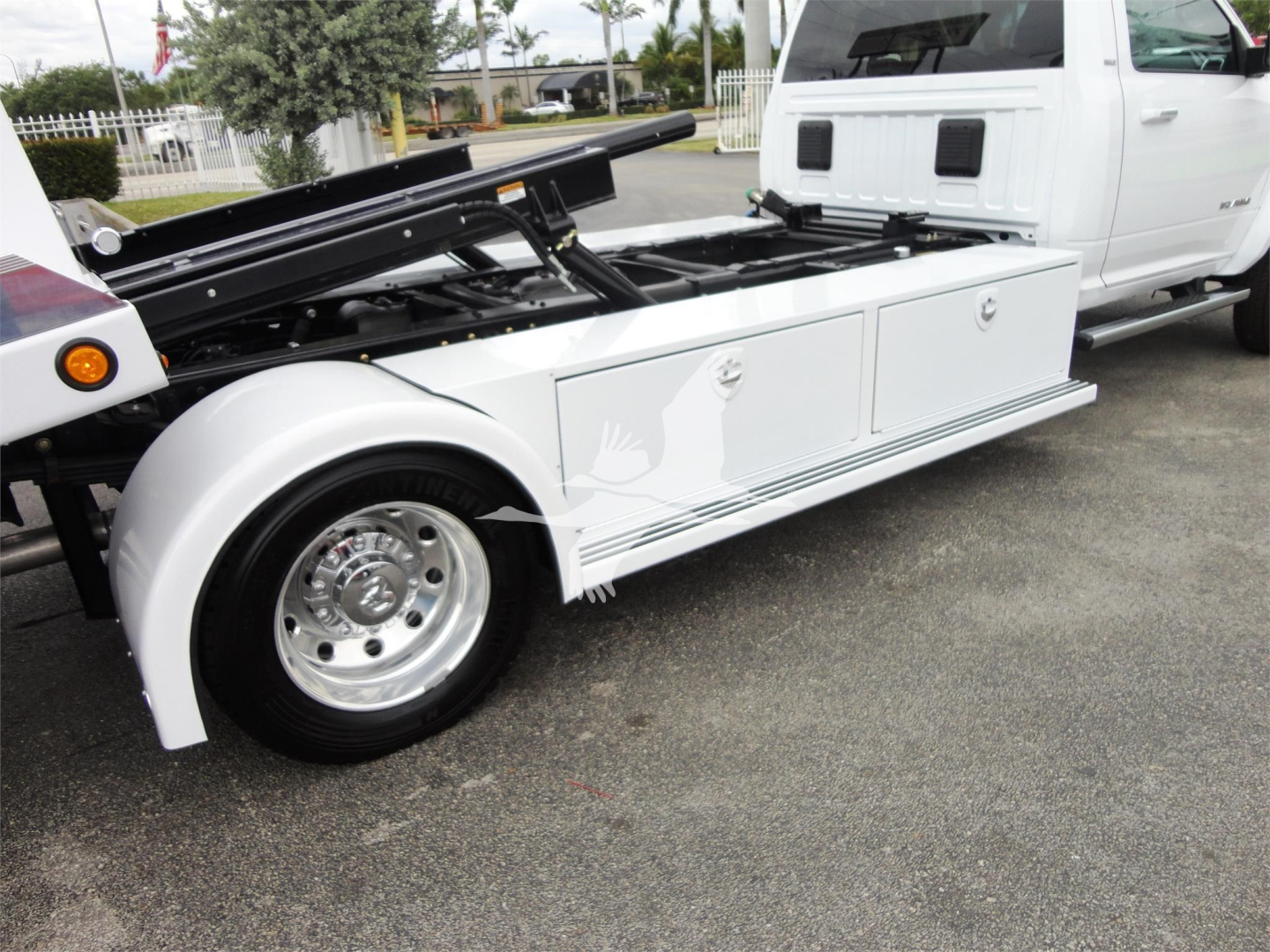Ram 5500 rollback tow truck with white utility bed, hydraulic equipment and compartments visible on side.
