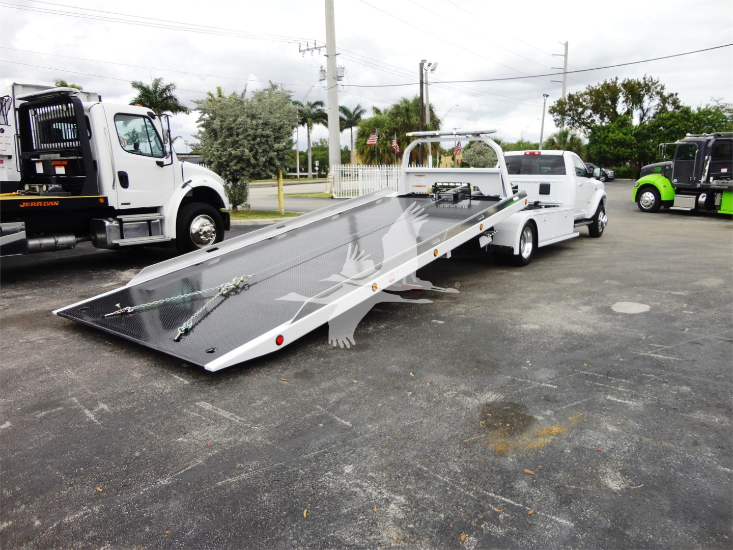 2023 Ram 5500 HD SLT roll-back truck with wedge-style flatbed and loading ramps, side rails, and tow hitch seen in a dealership lot.