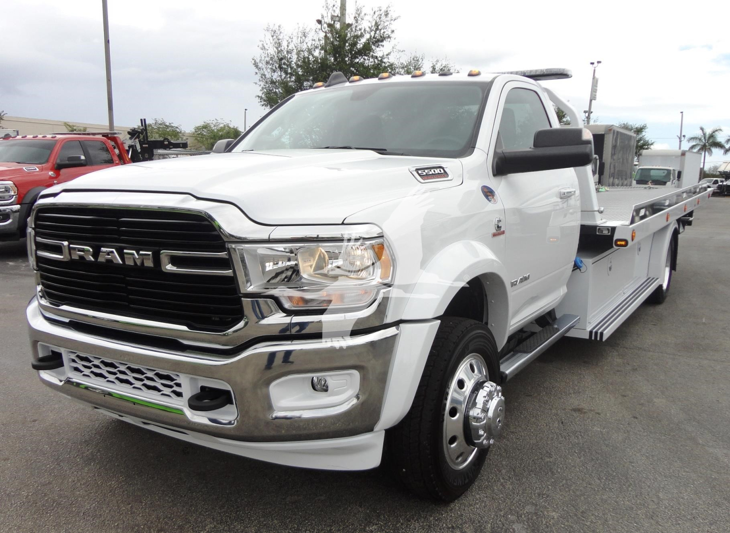 Ram 5500 rollback tow truck in white with chrome grille and flatbed side view showing large dual rear tires and towing equipment.