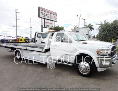 Ram 5500 rollback tow truck with flatbed and chrome wheels in a dealership lot.
