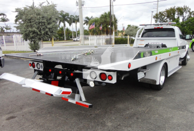 Ram tow truck with a large flatbed, showing rear bumper with reflective bars and diamond plate deck; no visible text legible on truck body.