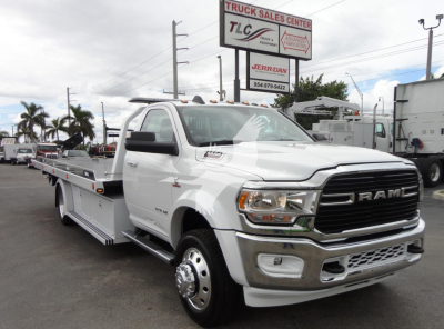 Ram 5500 heavy-duty rollback tow truck in white, front grille with RAM emblem, side view showing flatbed and dual rear wheel, dealership lot in background.