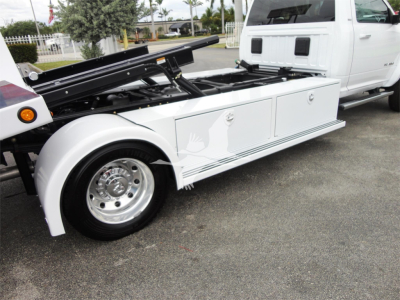 Ram 5500 rollback tow truck with white utility bed, hydraulic equipment and compartments visible on side.