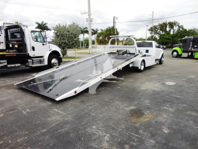 2023 Ram 5500 HD SLT roll-back truck with wedge-style flatbed and loading ramps, side rails, and tow hitch seen in a dealership lot.