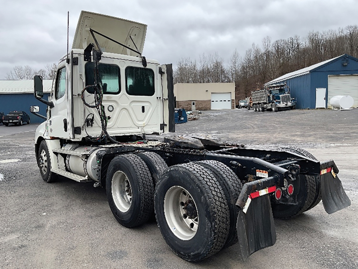 Freightliner Cascadia126 tractor rear view showing dual rear axles and fifth wheel, white cab, multiple mirrors, parked lot.