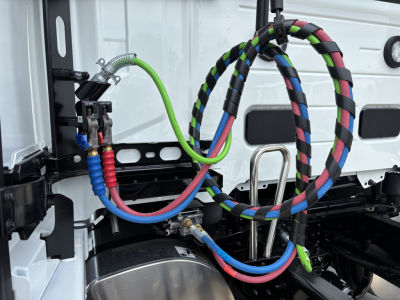 Volvo VNL cab area showing colorful braided air lines and fittings; hoses labeled; metallic tank and surrounding white truck body.