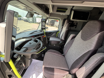 Interior of new Volvo VNL64T860 tractor cab showing driver seat and passenger seat, steering wheel, digital dashboard, mounted screens, and overhead storage.