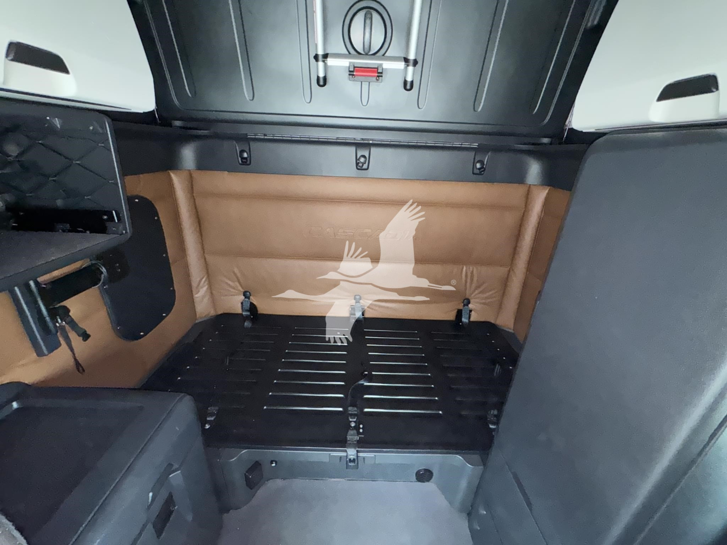 Freightliner Cascadia 126 sleeper cab cargo area showing tan rear paneling, black floor with ribbed mat, and side storage; limited interior view from rear.