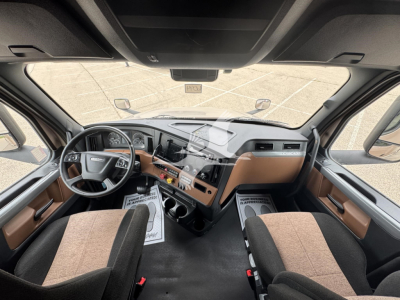 Cab interior of a 2023 Freightliner Cascadia 126 sleeper cab showing dashboard with brown and black trim, steering wheel, and two front seats.