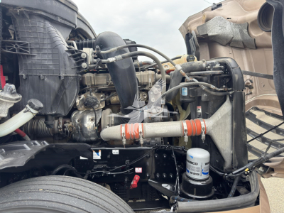 Truck engine bay of a Freightliner Cascadia showing coolant reservoir, oil filter, and various hoses and components under the hood.