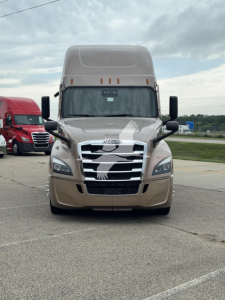 Front view of a Freightliner Cascadia sleeper cab truck with a chrome grille and beige paint, badge on hood, headlights, and side mirrors visible.