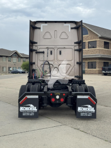 Rear view of a Freightliner Cascadia sleeper tractor showing the back of the cab and chassis with mud flaps and wiring harnesses visible.