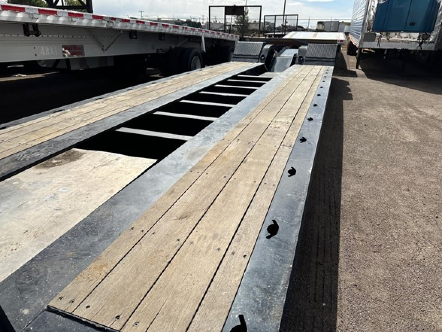 Flatbed trailer deck with wooden planks and metal frame, long lowboy trailer showing cutouts and fasteners along edge.