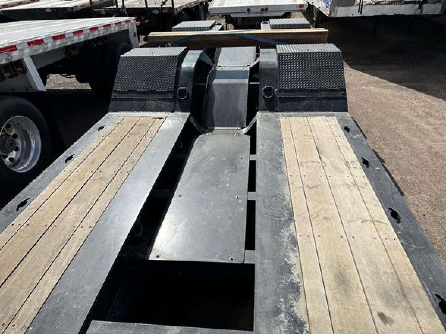 Trailer part showing TE110DG lowboy deck with wooden planks and metal frame, center slot access, rear coupling areas, and wheel wells visible.