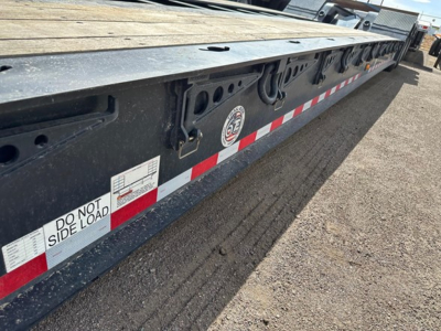 Trailing edge of a lowboy trailer showing Do Not Side Load label, reflective red/white striping, and circular GE logo plate with hooks and fittings along the side.