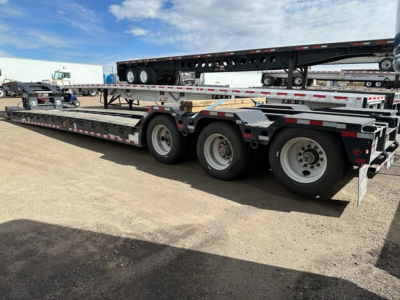 Trail-Eze TE110DG lowboy trailer showing dual rear axles and flatbed with accessories and a stretched upper trailer in background.