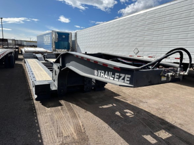 Trail-Eze TE110DG lowboy trailer showing side with Trail-Eze logo and metal deck, with blue equipment on front and clear sky.