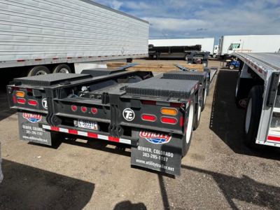 Trailer rear view showing TE110dg lowboy trailer with flatbed and ramps in a used equipment lot.