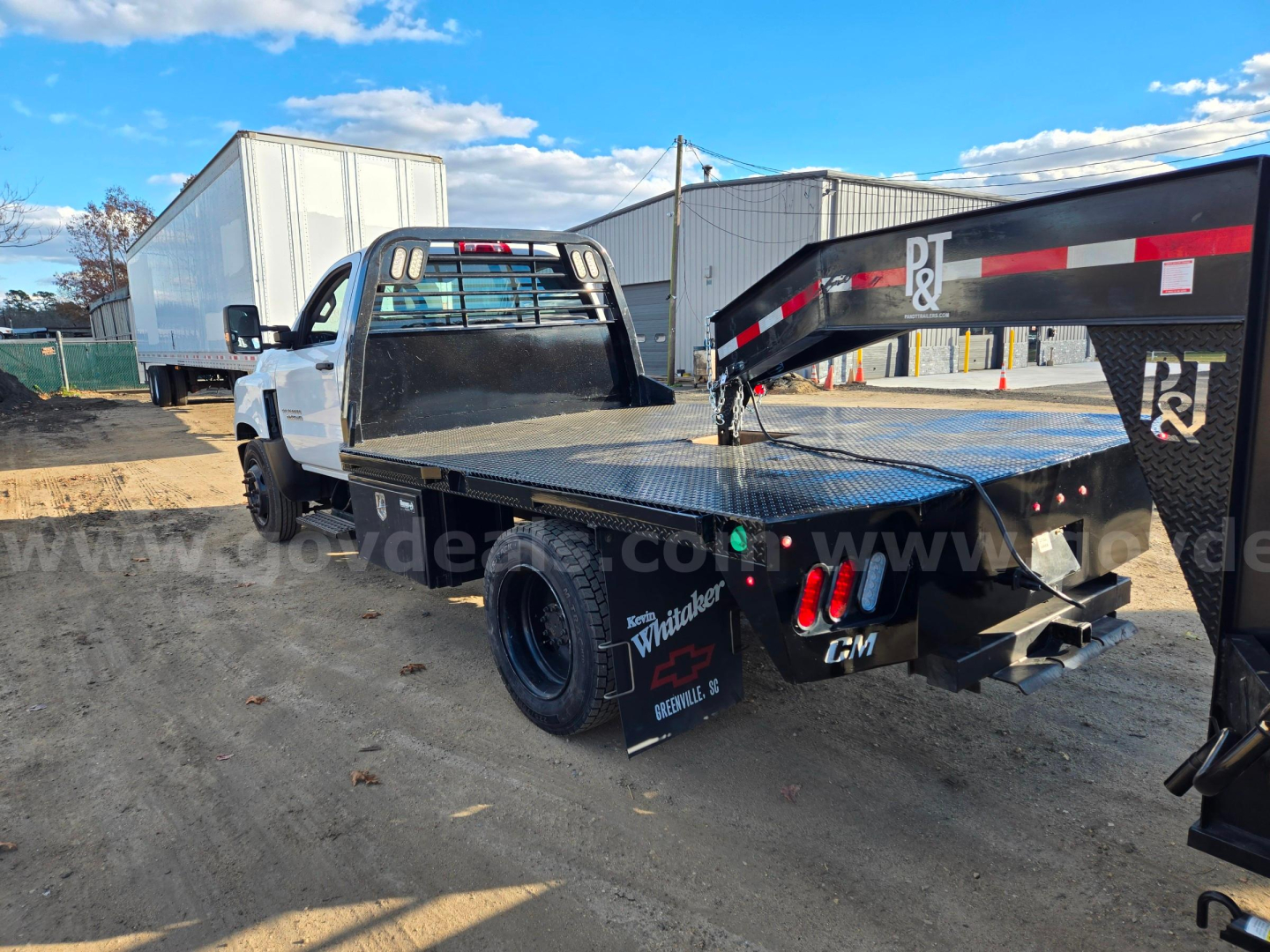 Flatbed tow truck chassis with black metal flatbed and dual rear wheels, white cab, heavy-duty rear bumper, and tail lights; visible branding on fenders and equipment, Chevrolet logo on emblem near rear