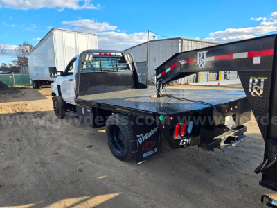 Flatbed tow truck chassis with black metal flatbed and dual rear wheels, white cab, heavy-duty rear bumper, and tail lights; visible branding on fenders and equipment, Chevrolet logo on emblem near rear