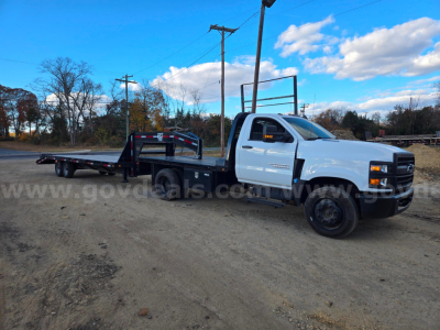 Flatbed tow truck in a gravel lot with white cab and black flatbed, Chevrolet badge visible.