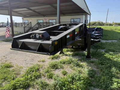 Chassis trailer frame showing black steel box with low profile, several access points and hydraulic connections; American flag and building in background.