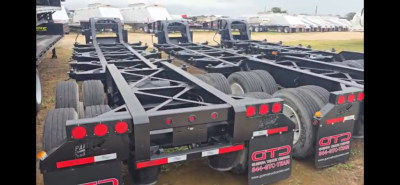 Chassis trailer frames in a dealership lot with multiple axles and red taillight assemblies visible.